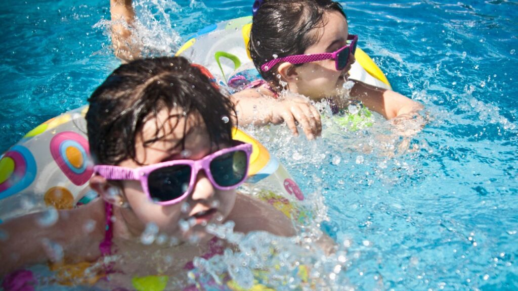 Two young children swimming and smiling in a pool on a sunny day