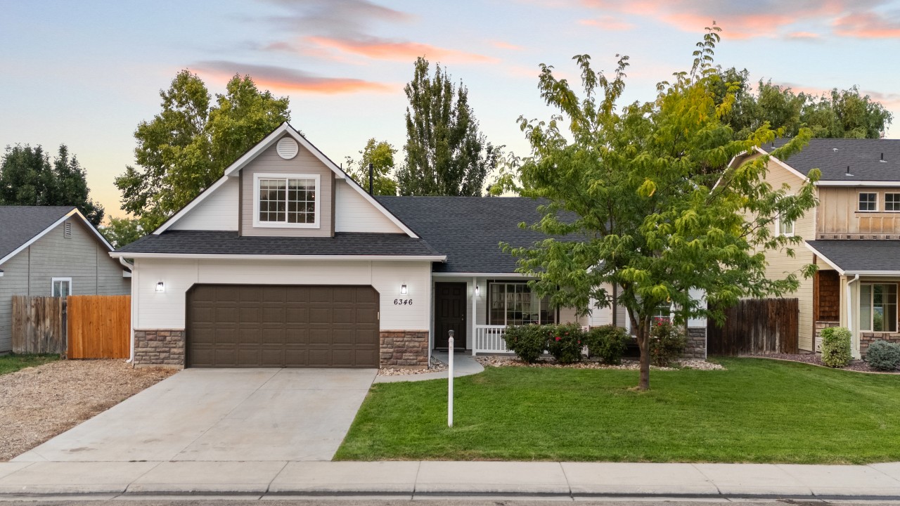 Charming single-level home in Nampa with covered front porch, two-car garage, manicured lawn, and mature trees.