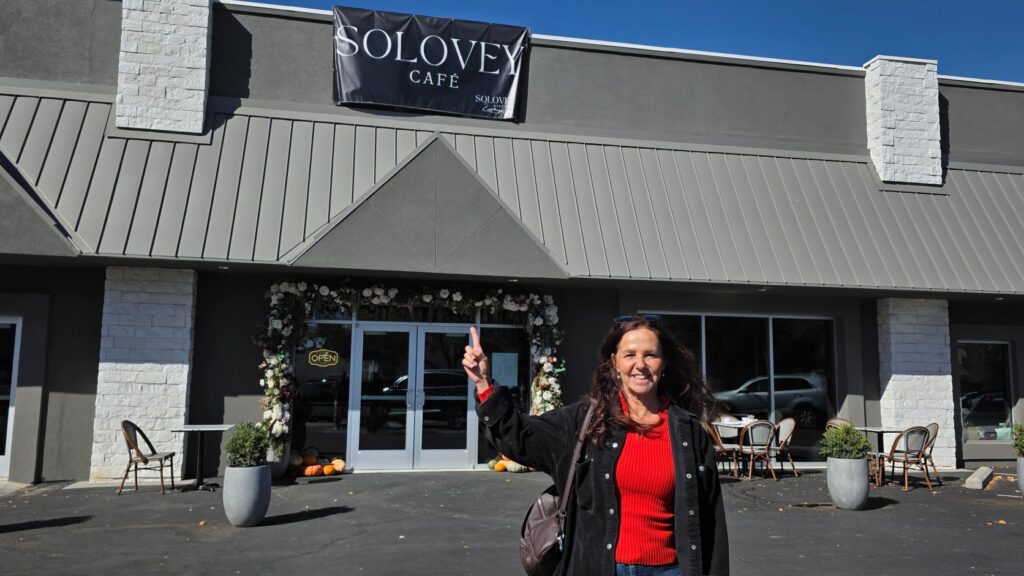Judit Crace of All Things Nampa pointing up at the Solovey Café sign on 13th Ave. S. in downtown Nampa
